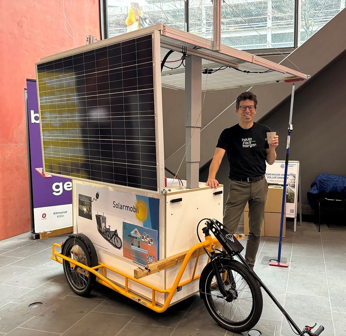 Mann steht mit Kaffeebecher in der Hand neben dem Solarmobil