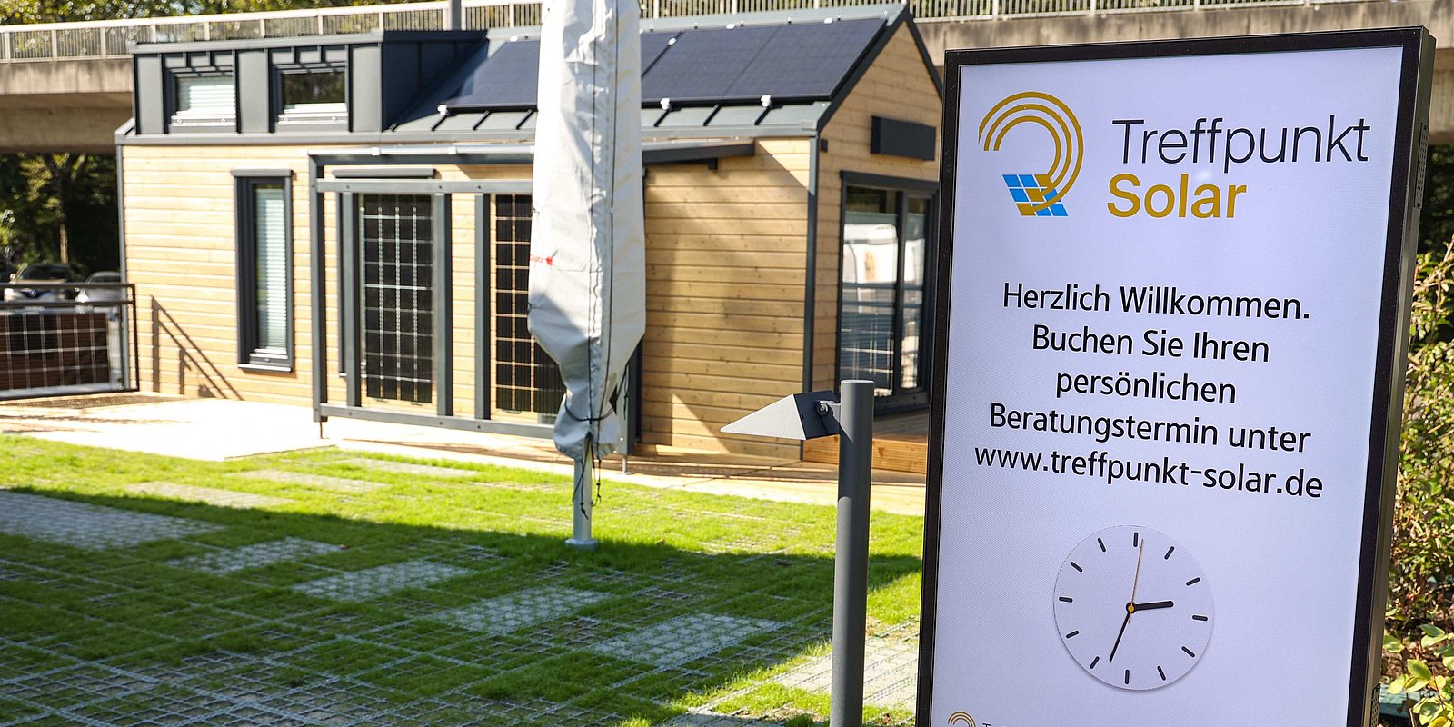 Eine Infotafel von "Treffpunkt Solar" vor einem Haus mit Photovoltaik